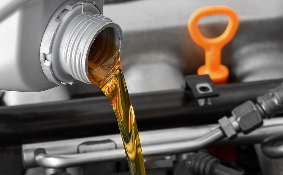 Motor oil being poured into a vehicle engine beside the dipstick.